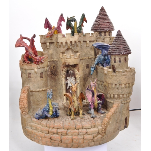 229 - A collection of four resin / plastic dragon light-up figures, comprising of a resin castle and drago... 