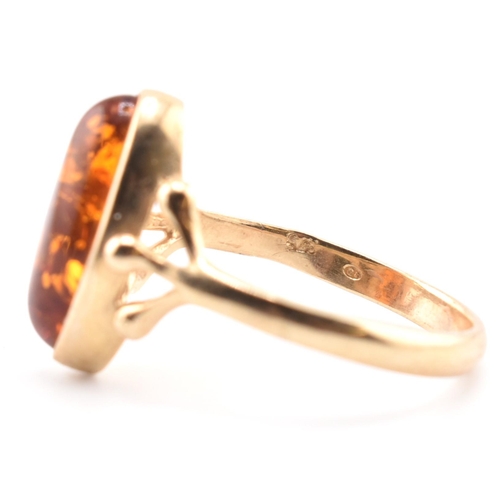 123 - A hallmarked 9ct gold and amber ring. The 9ct yellow gold ring set with a bezel set amber cabochon w... 