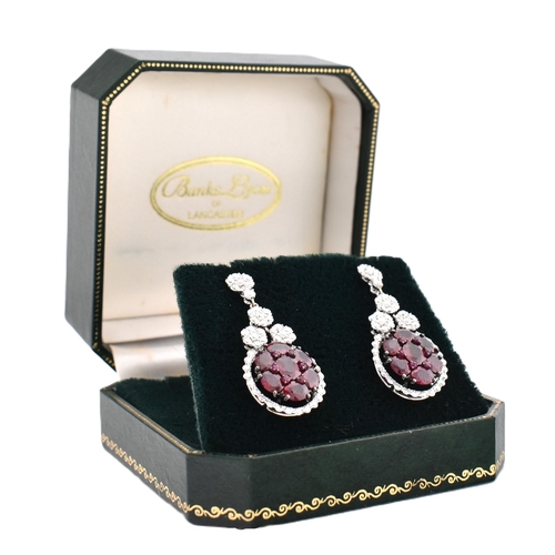 33 - A pair of 18ct gold ruby and diamond pendant earrings. The 18ct white gold earrings having a cluster... 