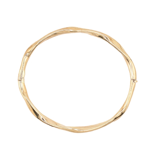 79 - A hallmarked 9ct gold hinged bangle cased. The 9ct yellow gold bangle having a twisted design with h... 