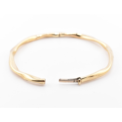 79 - A hallmarked 9ct gold hinged bangle cased. The 9ct yellow gold bangle having a twisted design with h... 