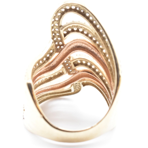 83 - A 9ct bi-colour gold and CZ swirl ring. The 9ct gold swirl ring having four yellow gold rows of pave... 