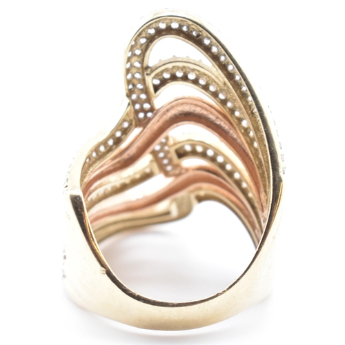 83 - A 9ct bi-colour gold and CZ swirl ring. The 9ct gold swirl ring having four yellow gold rows of pave... 