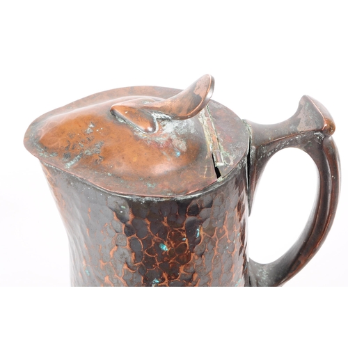 382 - An early 20th century Arts & Crafts hand hammered copper ewer jug. The jug having hinged lid ato... 