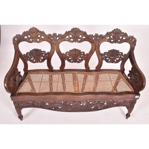 545 - An Indo - Portuguese manner hardwood and cane hall bench. The bench having a carved pierced back res... 