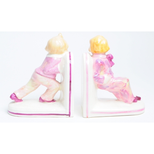 132 - Pair of 1930s art deco porcelain bookends depicting two children dressed in pink clown outfits. Both... 