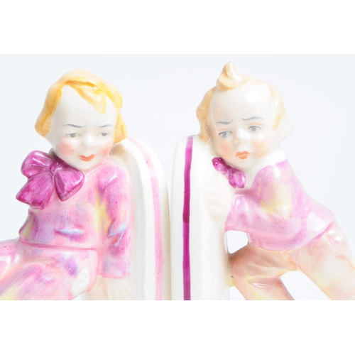 132 - Pair of 1930s art deco porcelain bookends depicting two children dressed in pink clown outfits. Both... 