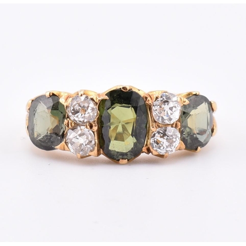 15 - A gold green sapphire and diamond three stone ring. The ring set with a central oval cut green sapph... 