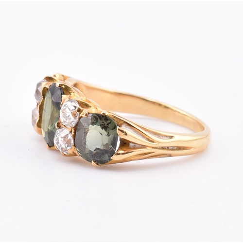 15 - A gold green sapphire and diamond three stone ring. The ring set with a central oval cut green sapph... 