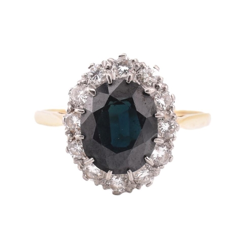 323 - An 18ct gold sapphire and diamond cluster ring. The ring set with an oval cut sapphire framed by twe... 