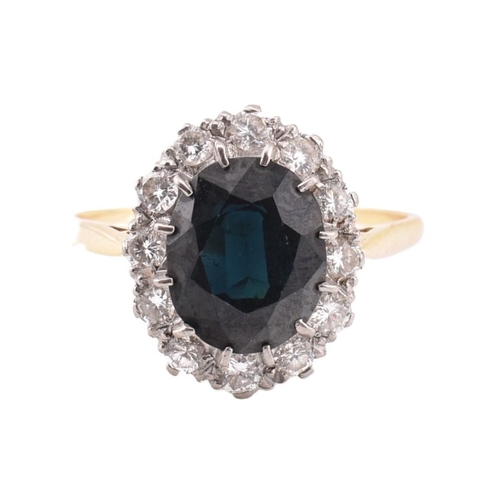 323 - An 18ct gold sapphire and diamond cluster ring. The ring set with an oval cut sapphire framed by twe... 