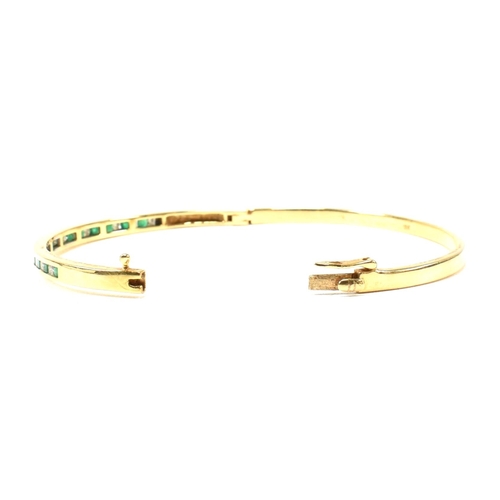 392 - An 18ct gold, emerald and diamond hinged bangle. The bangle having fifteen channel set princess cut ... 