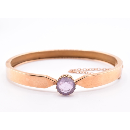 5 - A 15ct gold and amethyst bangle. The 15ct gold bangle set with a single claw mounted round cut ameth... 