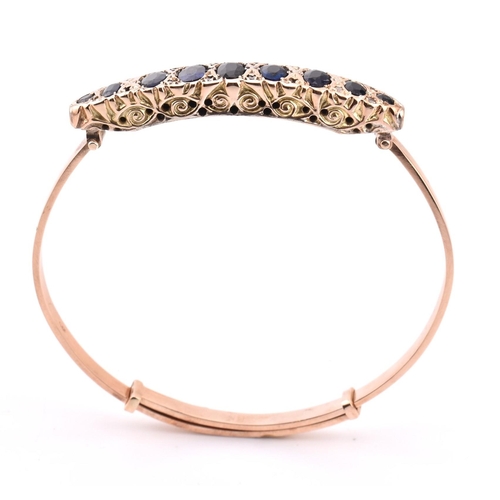 88 - An Edwardian 9ct gold and gem set bangle. The bangle set with 9 graduating oval cut gems including s... 