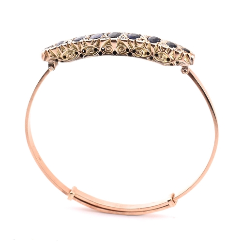 88 - An Edwardian 9ct gold and gem set bangle. The bangle set with 9 graduating oval cut gems including s... 