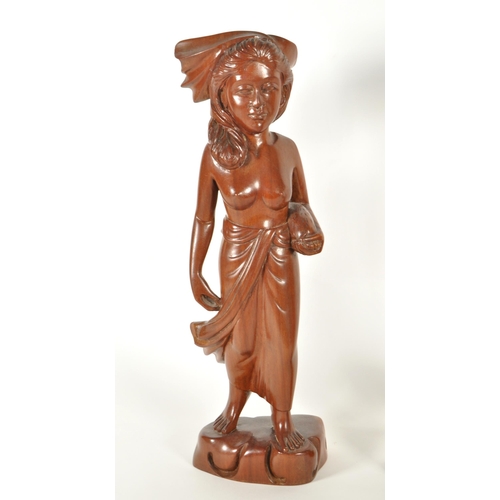 213 - Two 20th century Balinese carved wooden figures. Depicting a man and a woman raised on carved plinth... 