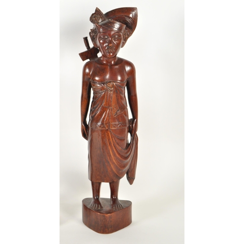 213 - Two 20th century Balinese carved wooden figures. Depicting a man and a woman raised on carved plinth... 