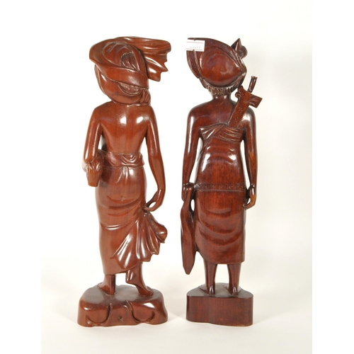 213 - Two 20th century Balinese carved wooden figures. Depicting a man and a woman raised on carved plinth... 