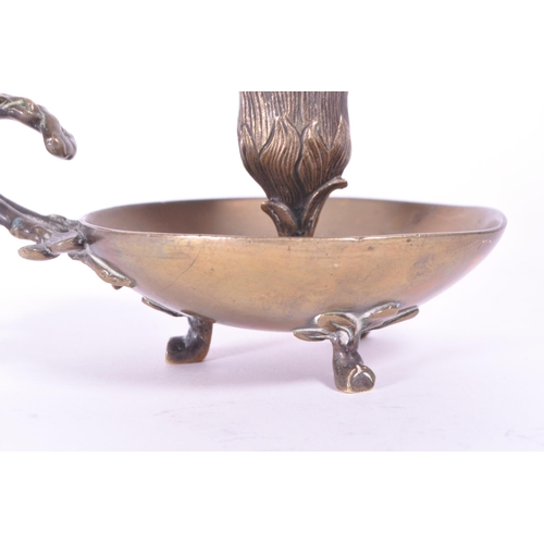 294 - A 19th century Art Nouveau brass candle holder / chamberstick. Foliate carry handle with bowl wax ru... 