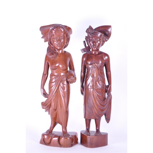 213 - Two 20th century Balinese carved wooden figures. Depicting a man and a woman raised on carved plinth... 