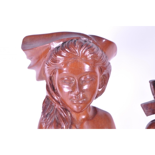 213 - Two 20th century Balinese carved wooden figures. Depicting a man and a woman raised on carved plinth... 