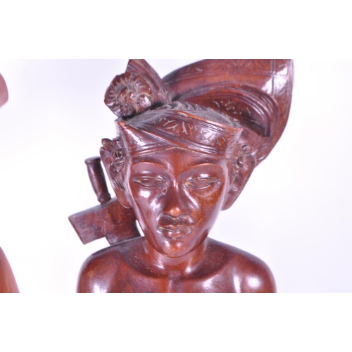 213 - Two 20th century Balinese carved wooden figures. Depicting a man and a woman raised on carved plinth... 