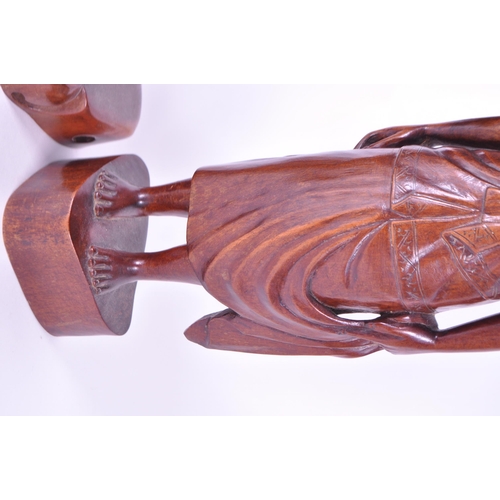 213 - Two 20th century Balinese carved wooden figures. Depicting a man and a woman raised on carved plinth... 