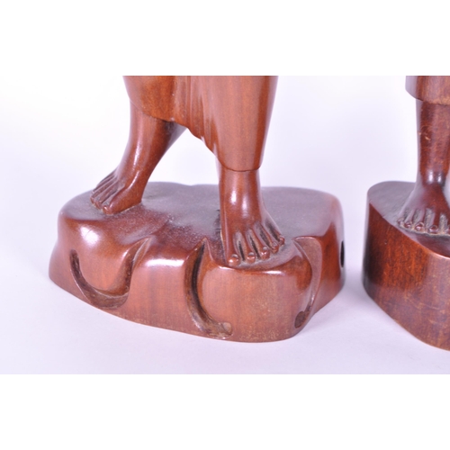 213 - Two 20th century Balinese carved wooden figures. Depicting a man and a woman raised on carved plinth... 