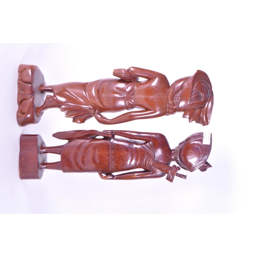 213 - Two 20th century Balinese carved wooden figures. Depicting a man and a woman raised on carved plinth... 