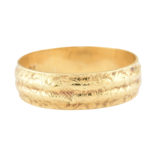 80 - An early 20th century gold bangle. The bangle with etched foliate and scroll decoration with a textu... 