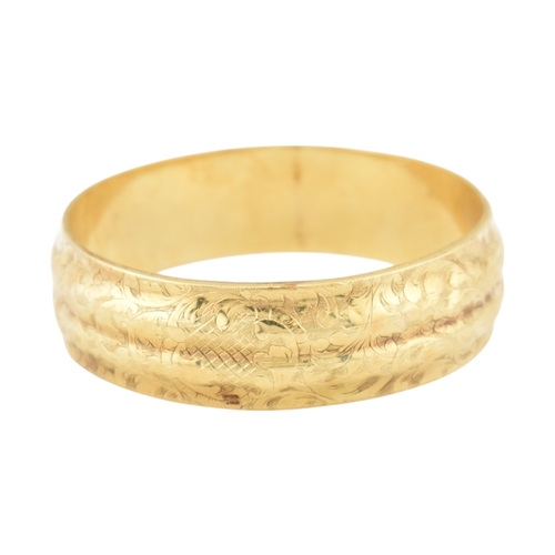 80 - An early 20th century gold bangle. The bangle with etched foliate and scroll decoration with a textu... 