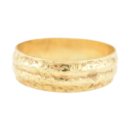 80 - An early 20th century gold bangle. The bangle with etched foliate and scroll decoration with a textu... 