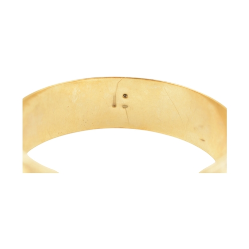 80 - An early 20th century gold bangle. The bangle with etched foliate and scroll decoration with a textu... 