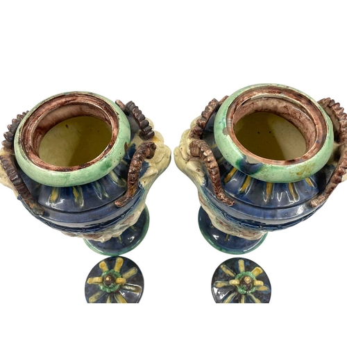 159 - A pair of late 19th century hand painted Majolica grotesque lidded urns. Each vase having a shaped l... 
